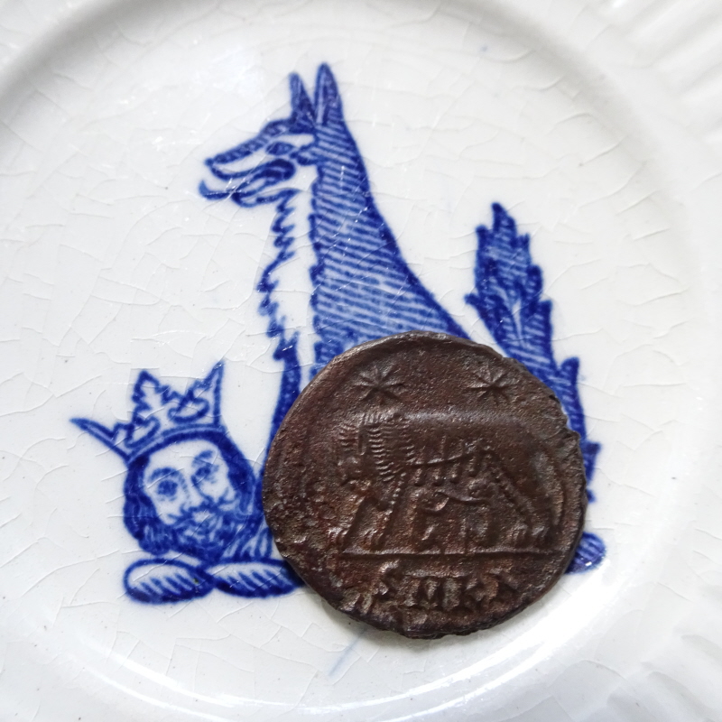 Wolf and Head Saucer and Roman coin with green patina, showing Romulus and Remus suckled by the She-Wolf. 