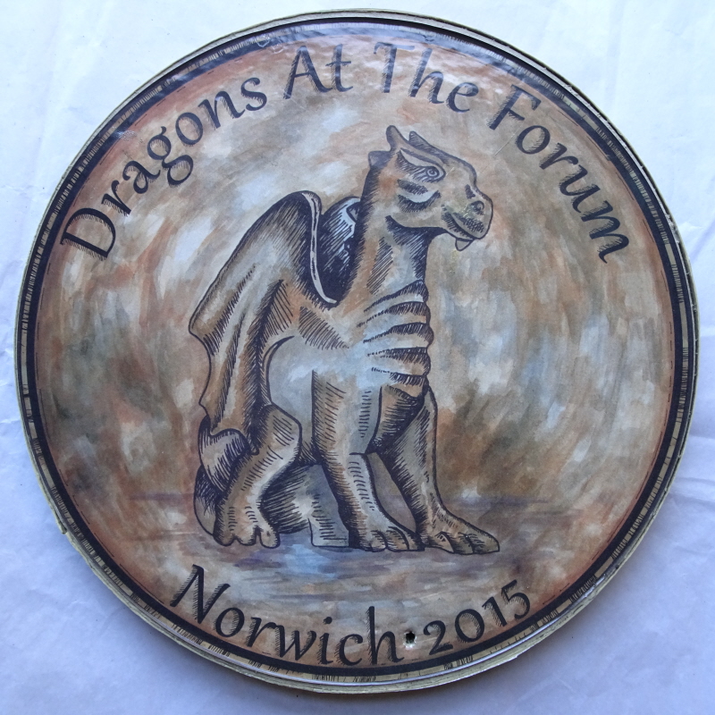 Card laminate display piece, designed to resemble a copper or gold coin, with a Dragon of the kind set up as art installations around Norwich in the 2015 Go-Go-Dragons Festival. The text around the edge reads "Dragons at the Forum Norwich 2015".