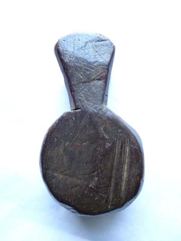 Carved wooden amulet, round with roughly triangular top piece with a hole for a cord to hang it around an animal's neck.