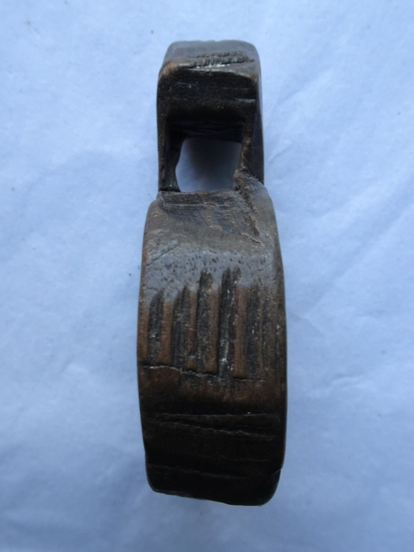 Carved wooden amulet, round with roughly triangular top piece with a hole for a cord to hang it around an animal's neck.