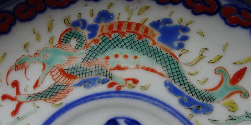 Detail of the saucer showing a two-legged, three-clawed green Dragon, with cross-hatching in black, highlights in red, and blue and yellow marks around.