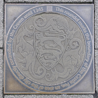A modern replica of the plaques marking the boundary of Norwich Castle Fee, with Lions in the centre and Dragons (originally wyverns) around. The text around them says, "This roundel marks the boundary of the Castle Fee, an area of the city directly controlled by the Crown until 1345."