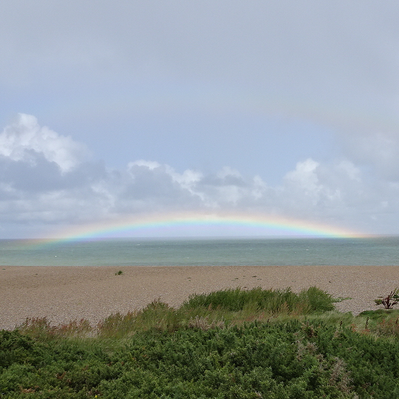 A rainbow over the sea at Salthouse in Norfolk, with glowing ends and a faint second arc above, beach in foreground and clouds above.